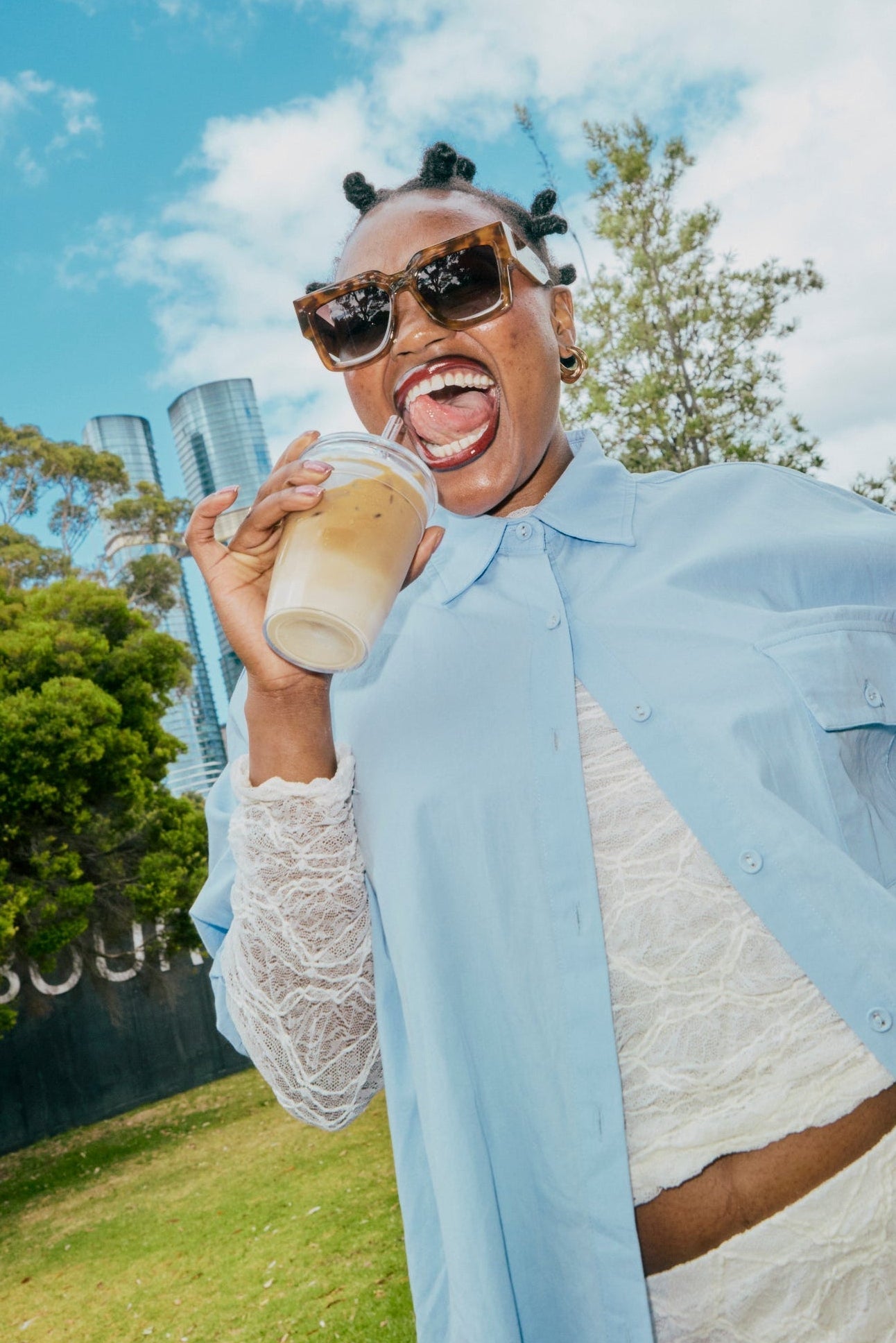 Person holding a drink and a cold cup outdoors with trees and blue sky in the background