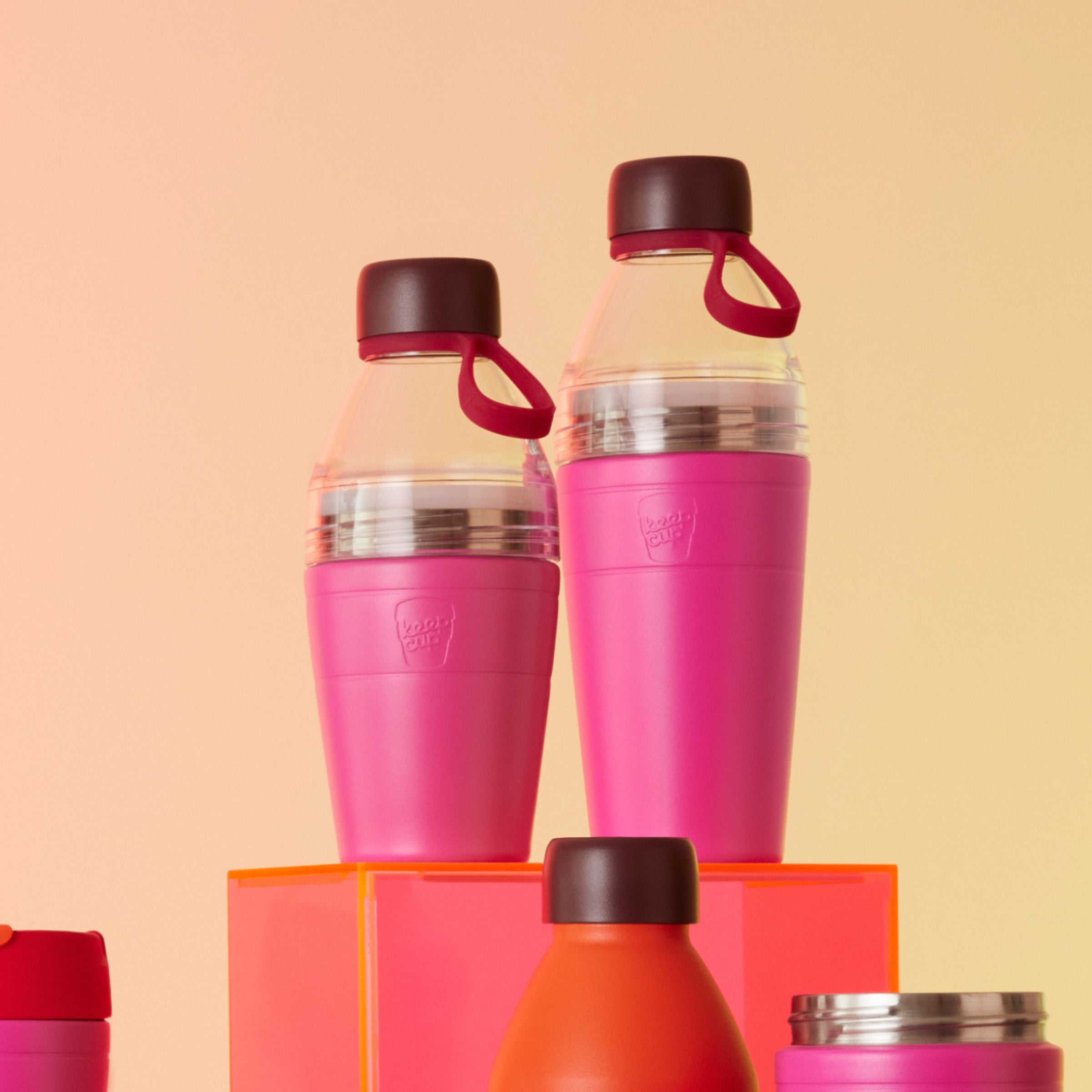 Two Pink KeepCup water bottles on an orange stand and peach background