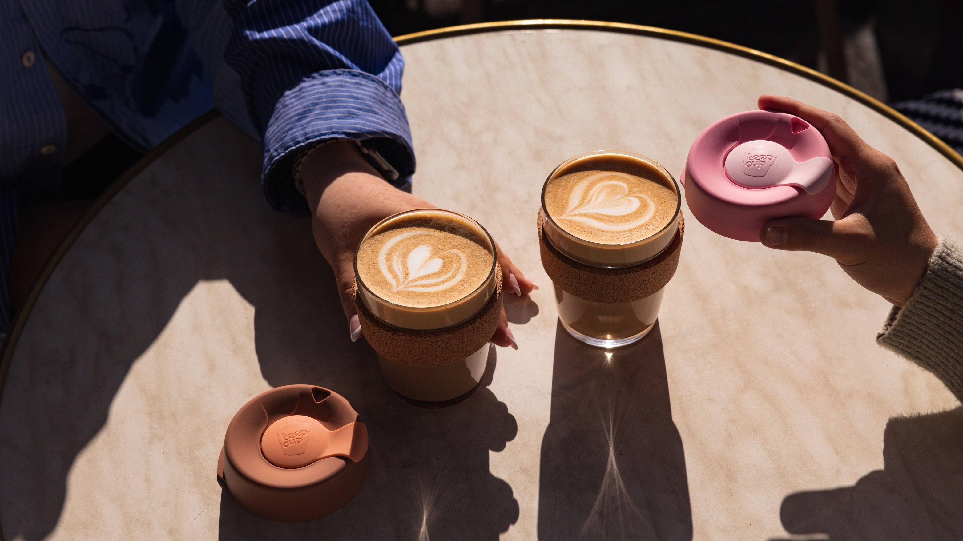 two coffee cups with latte art on a table, one being picked up by a hand.