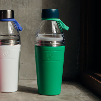 Green and white KeepCup water bottles with silicone carry bands on a concrete surface.