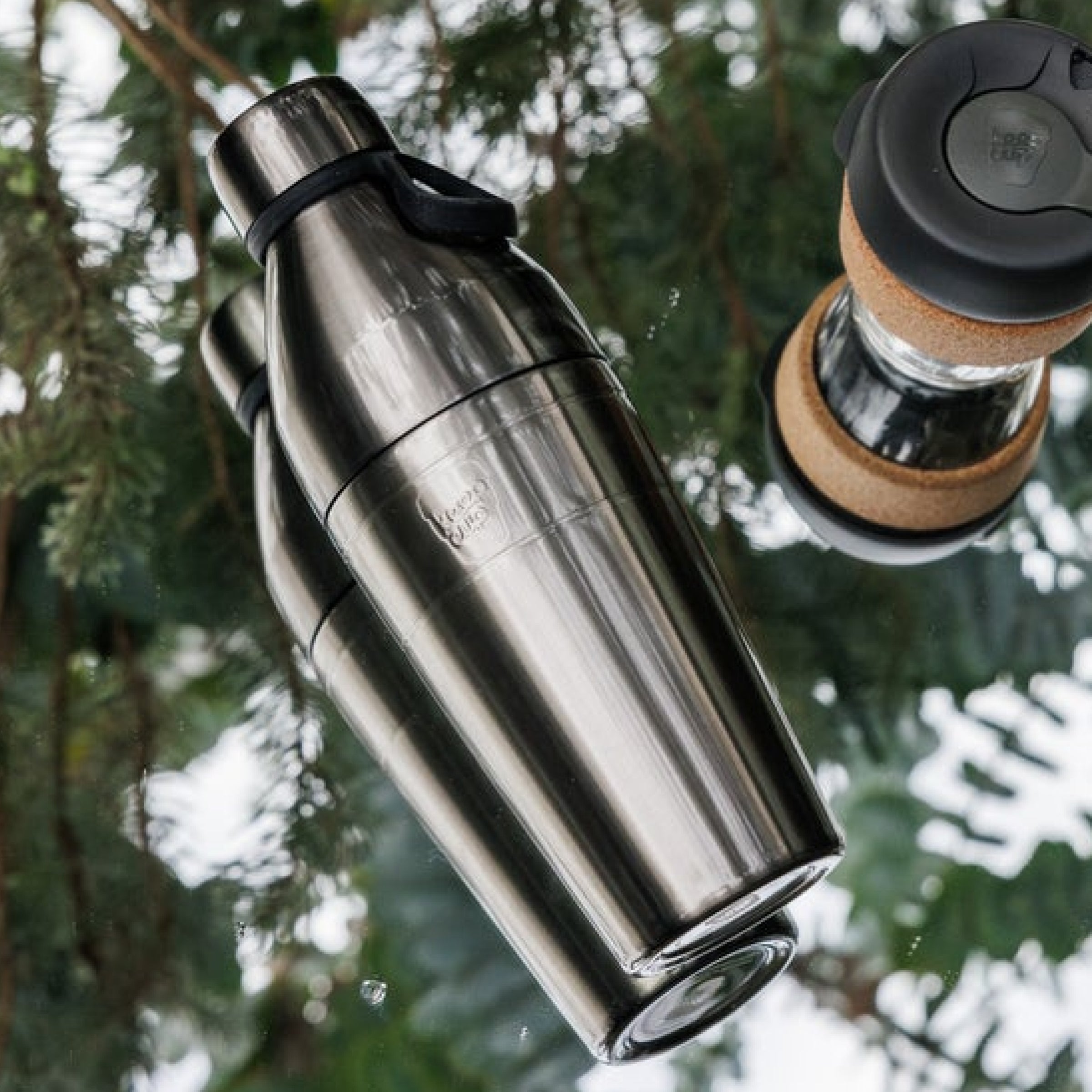 KeepCup Nitro insulated water bottle with black cap. Alongside a small brew cork reusable coffee cup against a blurred green background