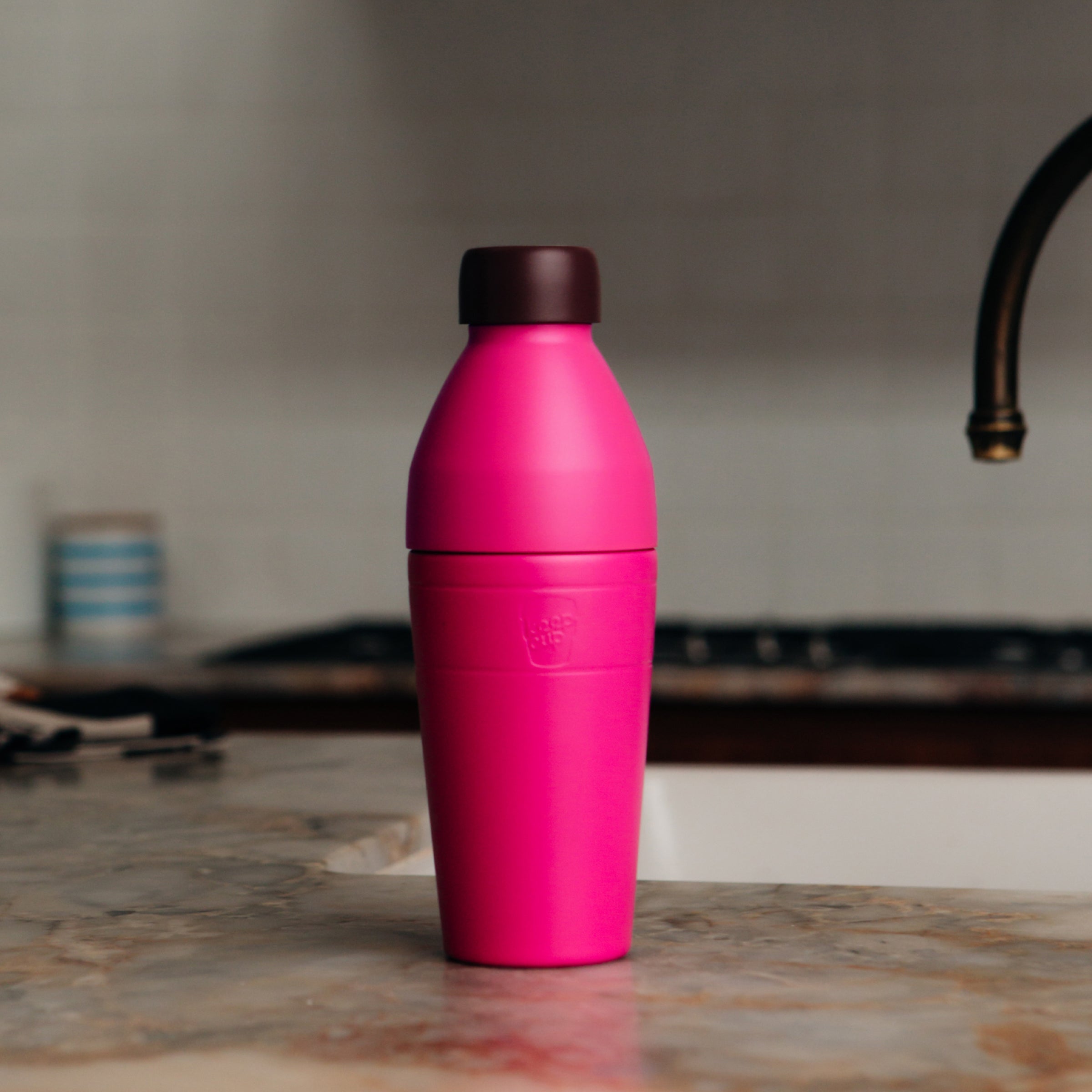 Pink KeepCup insulated water bottle on a kitchen counter with a blurred background