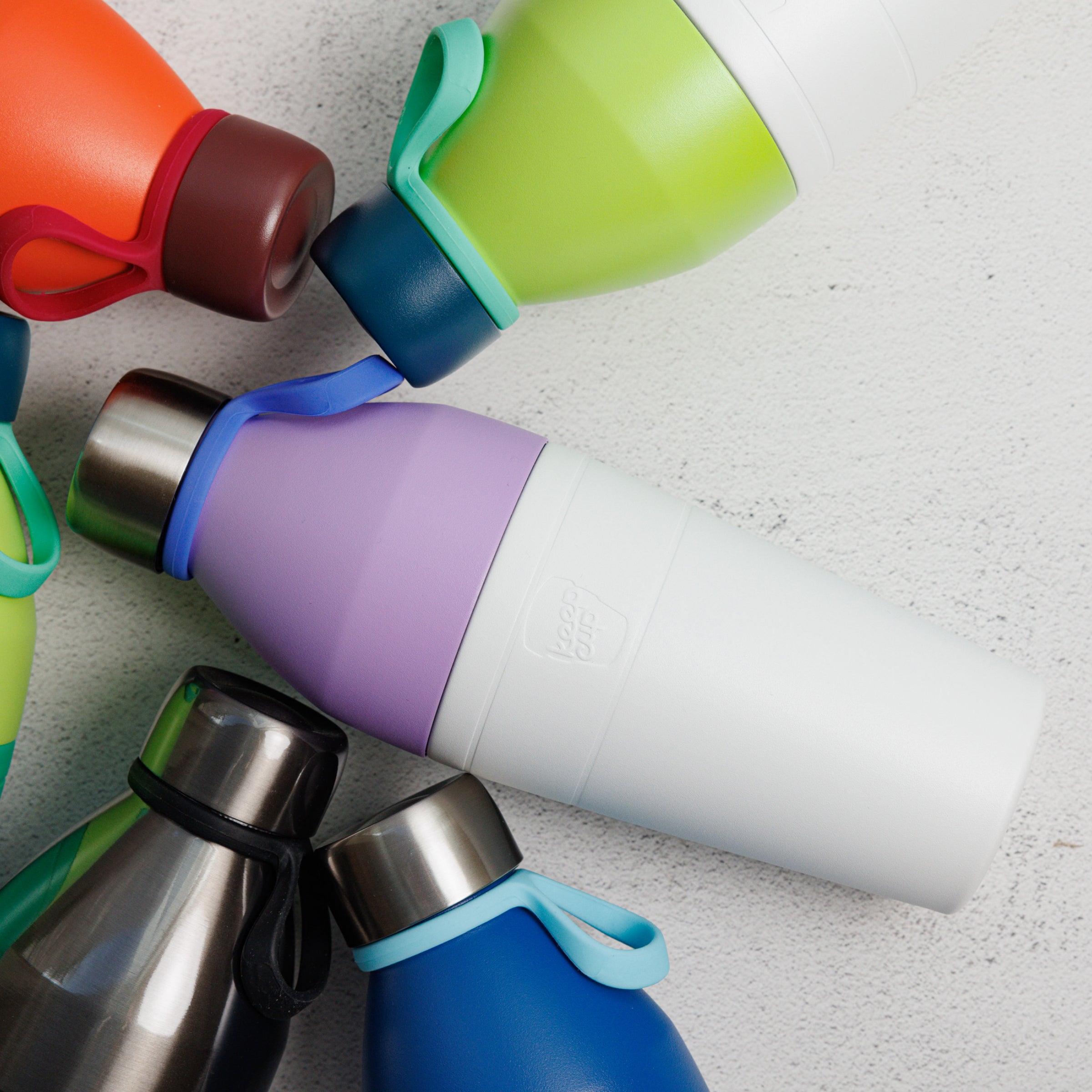 Colorful KeepCup water bottles layed out on a textured surface