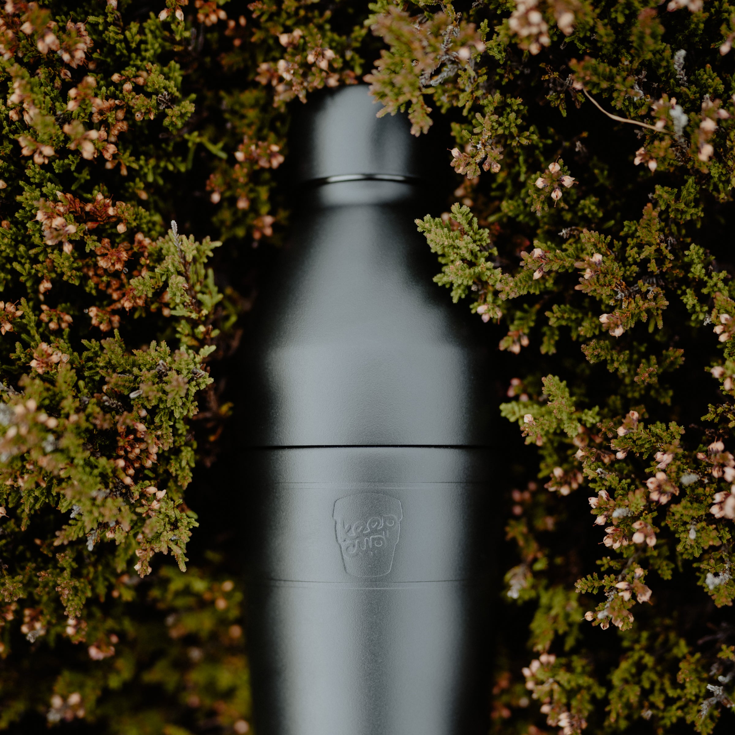 Black KeepCup insulated water bottle with a brand logo surrounded by green foliage