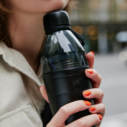 Person holding a black KeepCup water bottle with a blurred background