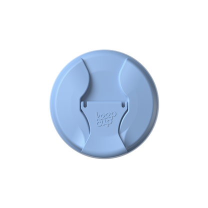 Top-down view of the KeepCup Commuter Flip Lid in Orchid, a light blue circular lid featuring a central flip-open drinking spout with the KeepCup logo embossed on the closure tab.
