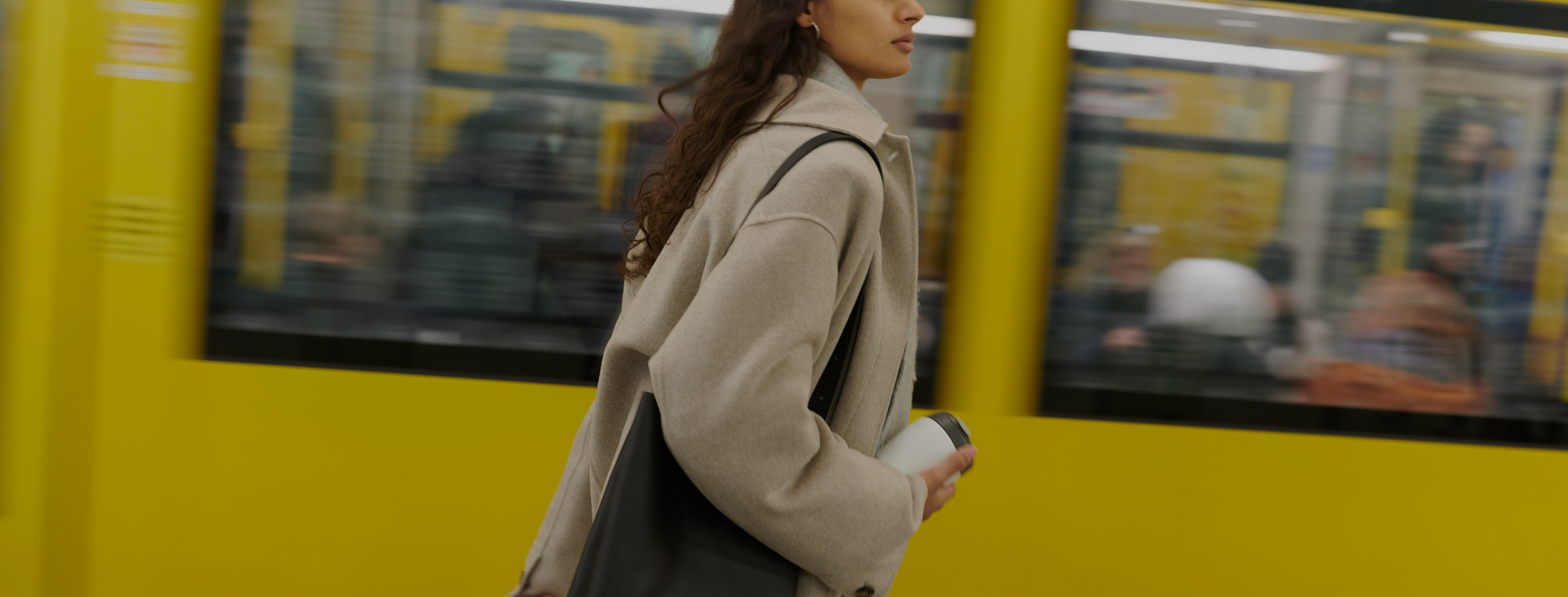 Woman walking past a yellow wall with blurred people in the background