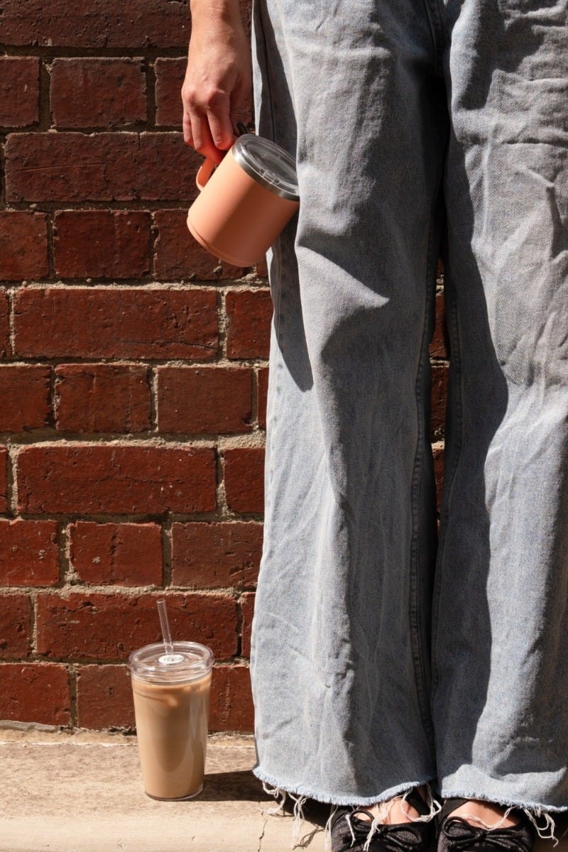 Woman holding KeepCup Camp Mug in Clay against brick wall with Cold Cup Original beside